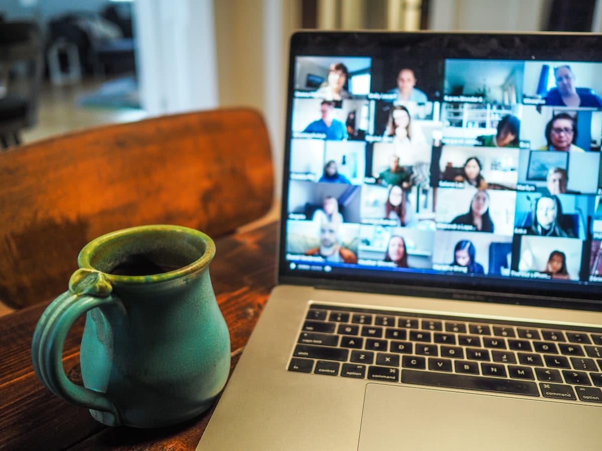 Laptop displaying a video conference call with multiple remote participants next to a coffee mug