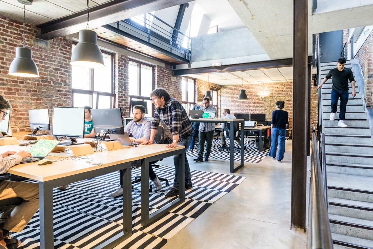 Open-plan loft coworking space with people at standing desks and exposed brick walls